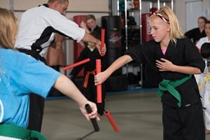 Two girls practice using nunchaku at a seminar at their dojo.